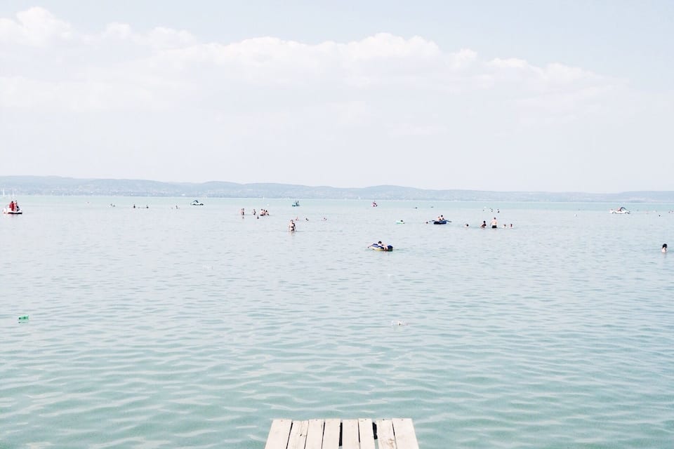 A wooden pier extending into calm waters with boats and people in the distance.