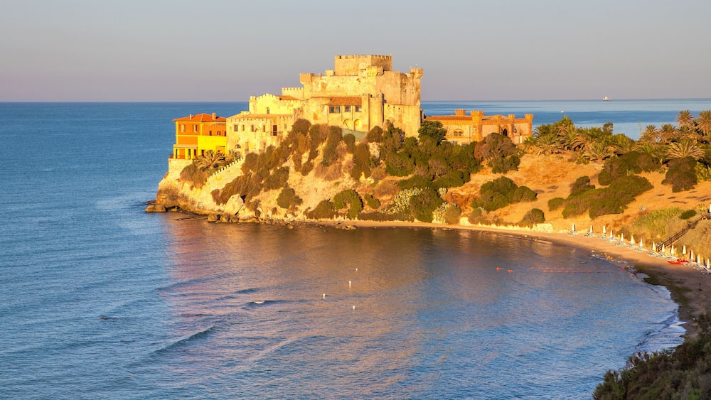 Un château situé sur la côte, avec une plage au premier plan.