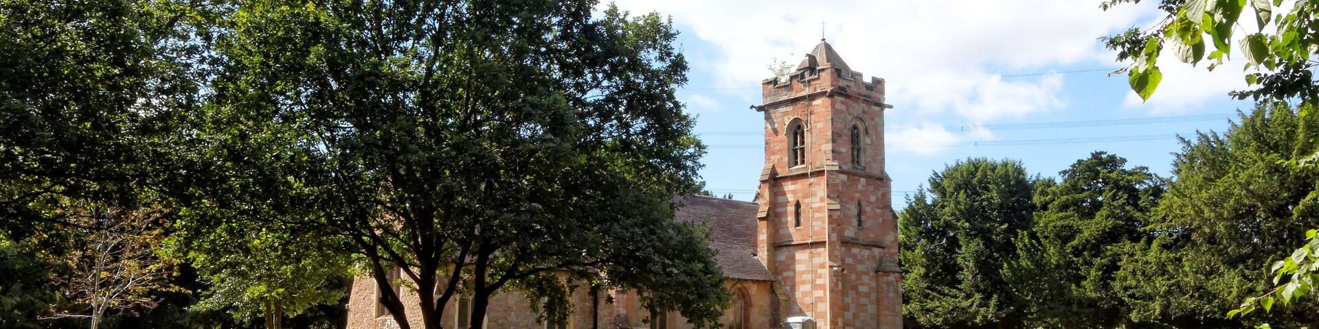 Una iglesia con una torre alta, rodeada de árboles y un cementerio.