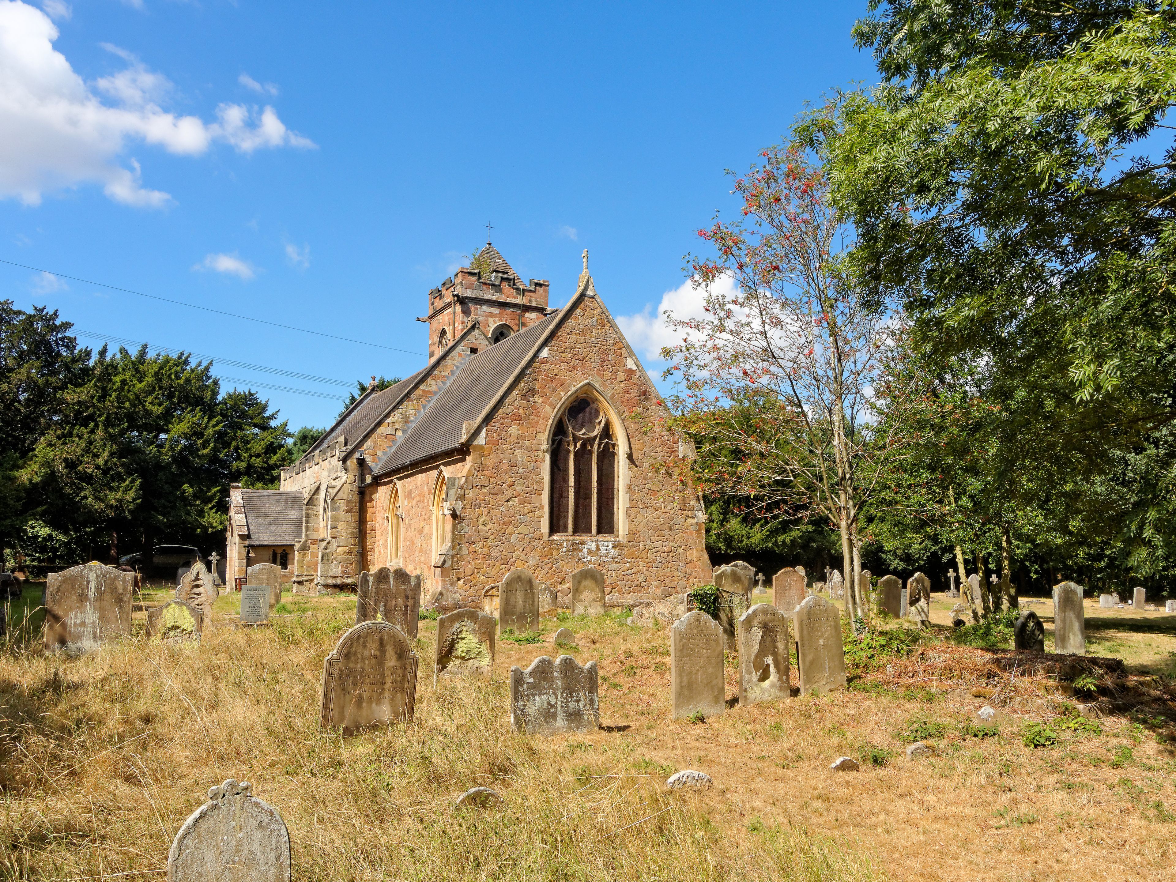 A church with a pointed roof and a bell tower, surrounded by a cemetery with numerous headstones.