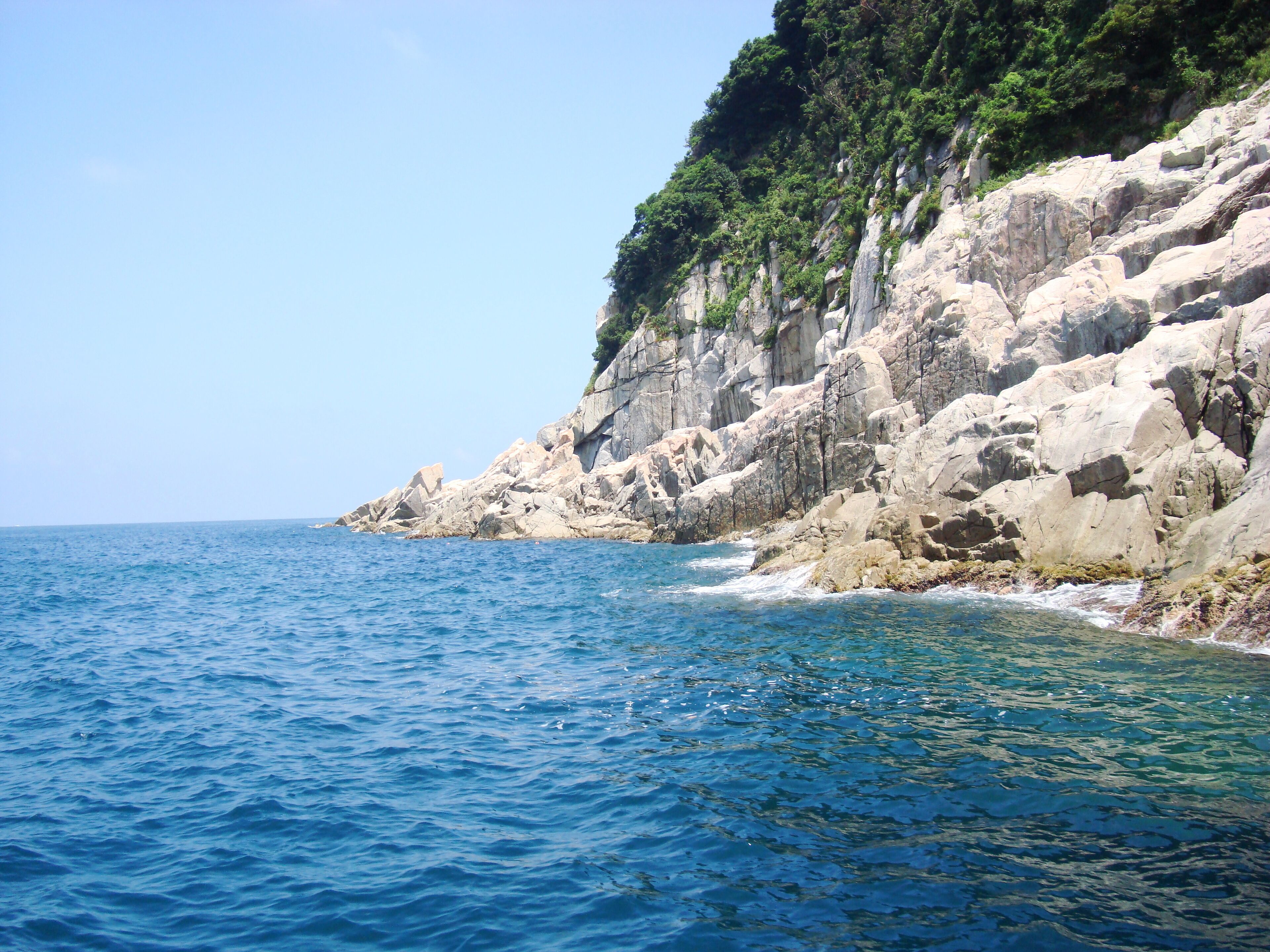 A rocky coastline with clear blue waters and lush greenery on the cliffs.