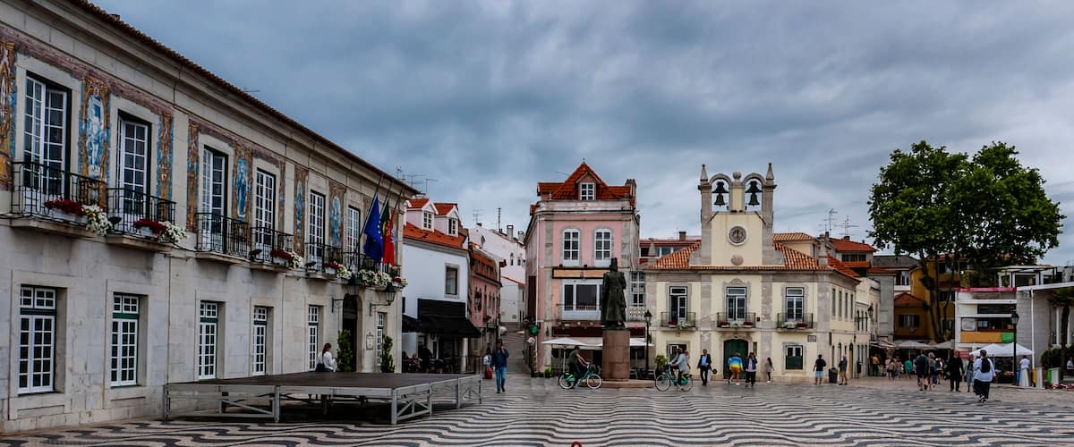 A historic square with tiled pavement, a prominent church with a bell tower, and traditional buildings with balconies.