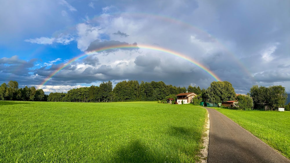 Ein üppiges, grünes Feld mit einem Regenbogen über einer ländlichen Landschaft.