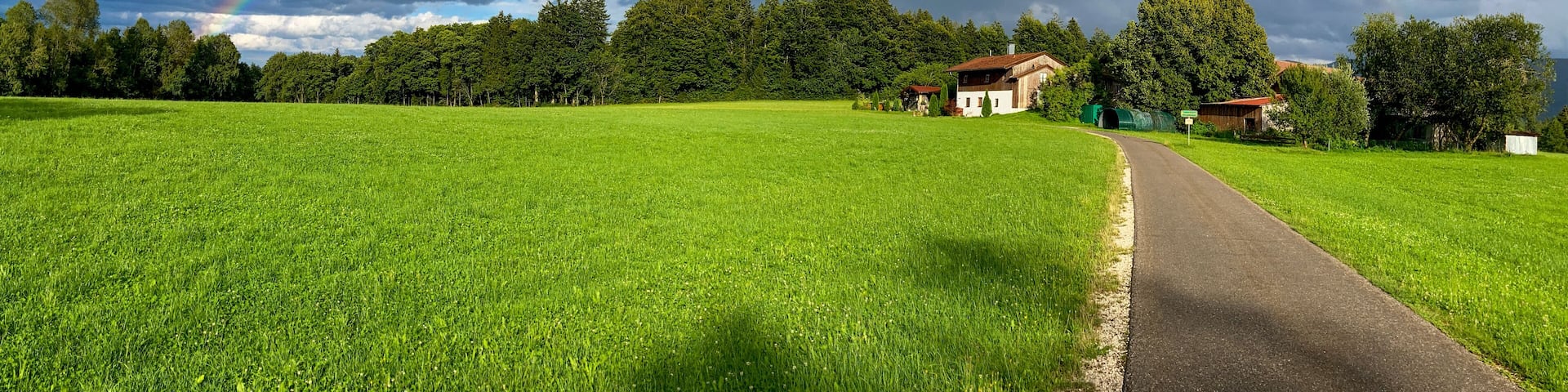 A lush green field with a rainbow arching over a rural landscape.