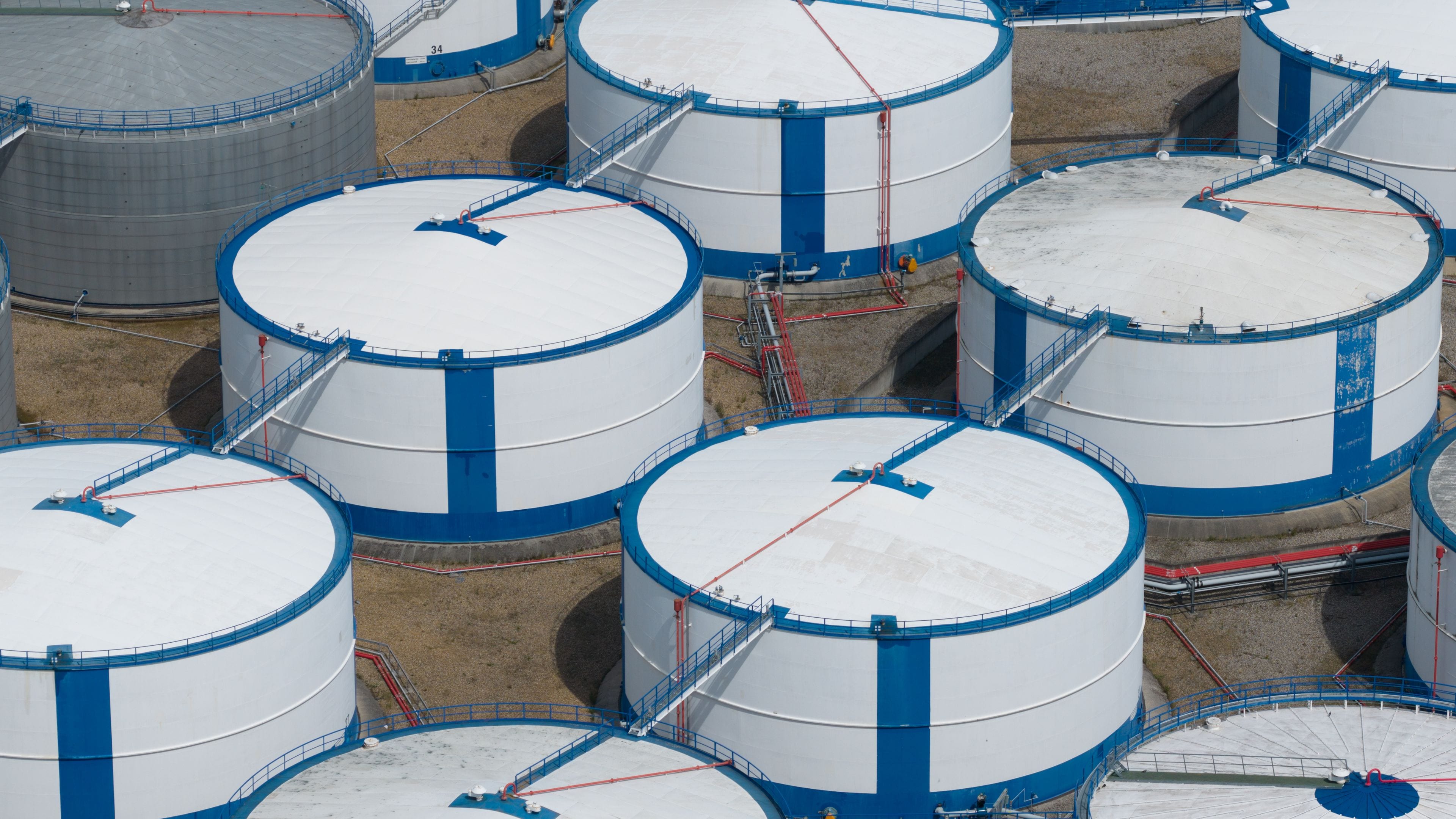 Een reeks grote, industriële opslagtanks in blauw en wit, gerangschikt in een complex patroon.