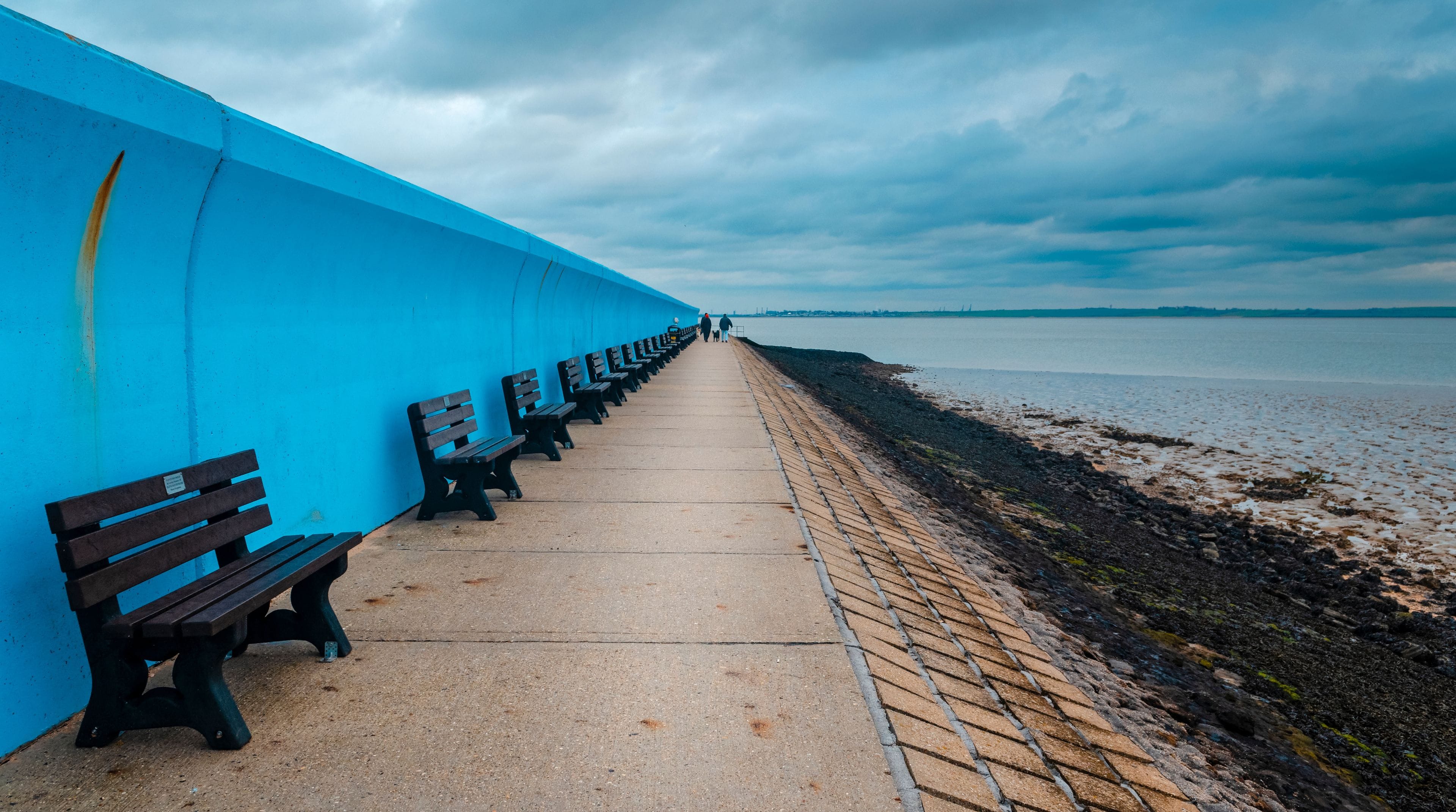 Een boulevard aan zee met banken en een blauwe muur.
