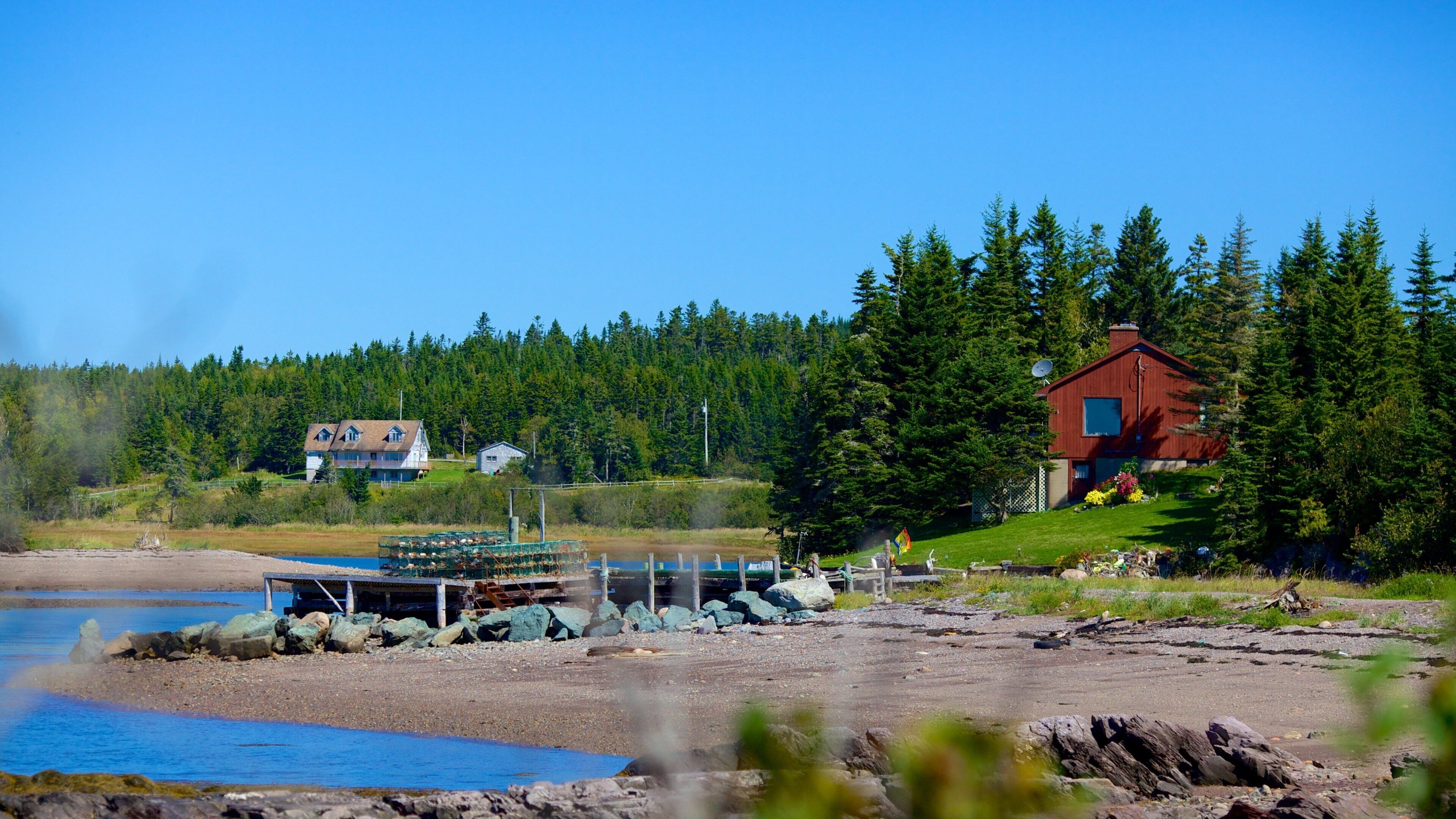 A coastal landscape with a wooden dock, a red house, and a forested hill.