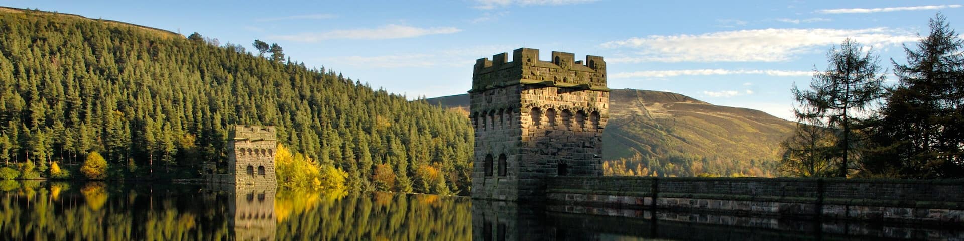 A castle on a lake with forested hills in the background.