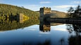 A castle on a lake with forested hills in the background.