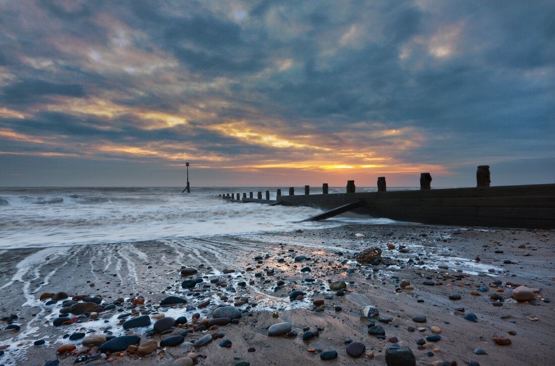 Une plage de galets, avec des vagues, au coucher du soleil.