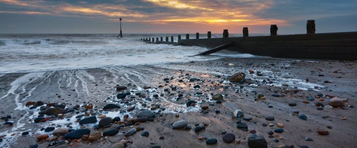 A beach with pebbles and waves at sunset.