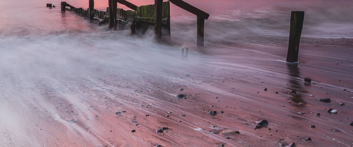 A wooden pier extending into a calm sea at sunset.