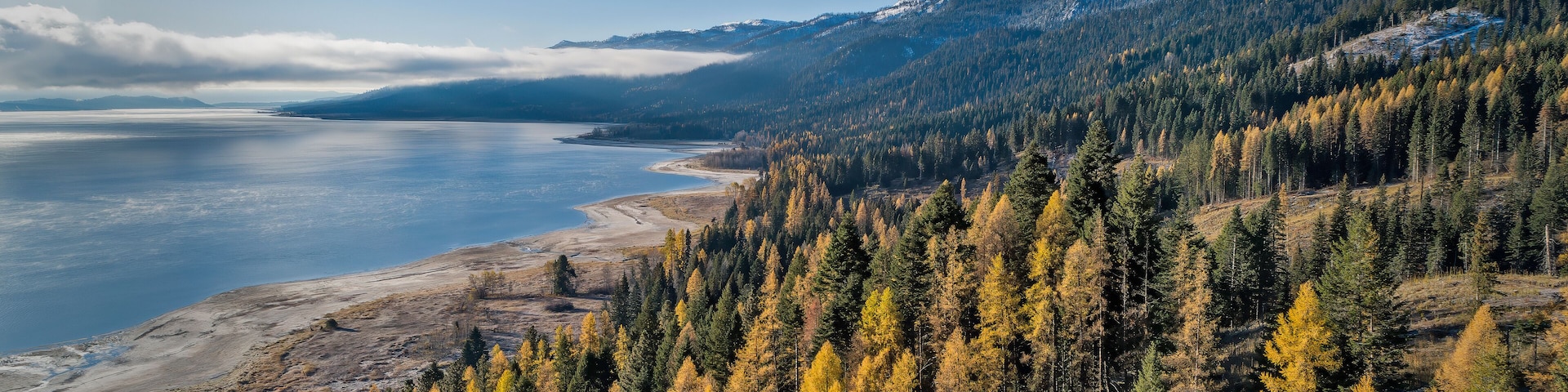 A mountainous landscape with a lake, autumn-colored trees, and snow-capped peaks.