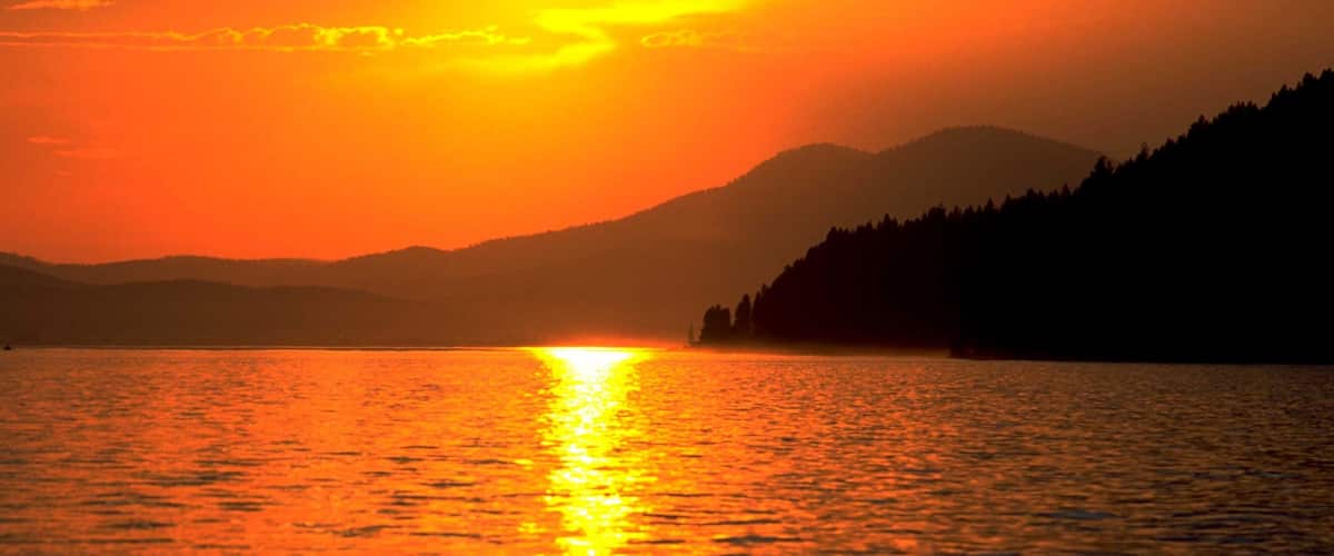 A sunset over a lake with mountains in the background.