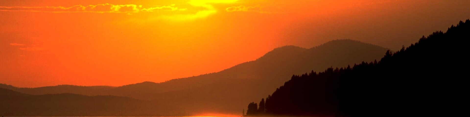 A sunset over a lake with mountains in the background.
