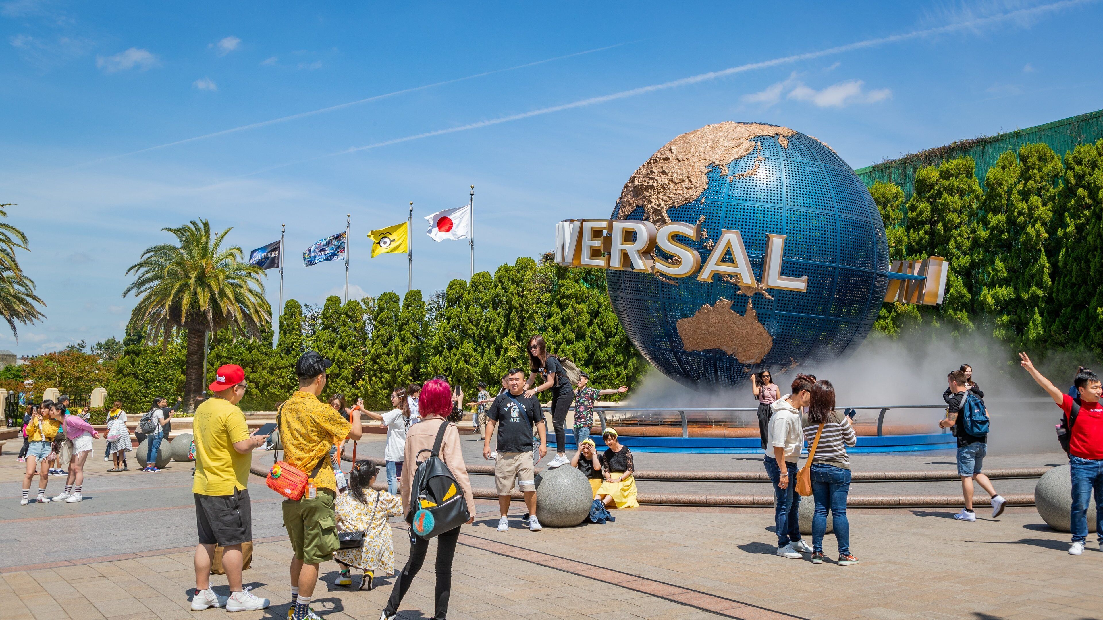 Un globo grande con 'VERSAL' y 'UNIVERSAL' escrito, rodeado de palmeras y gente.