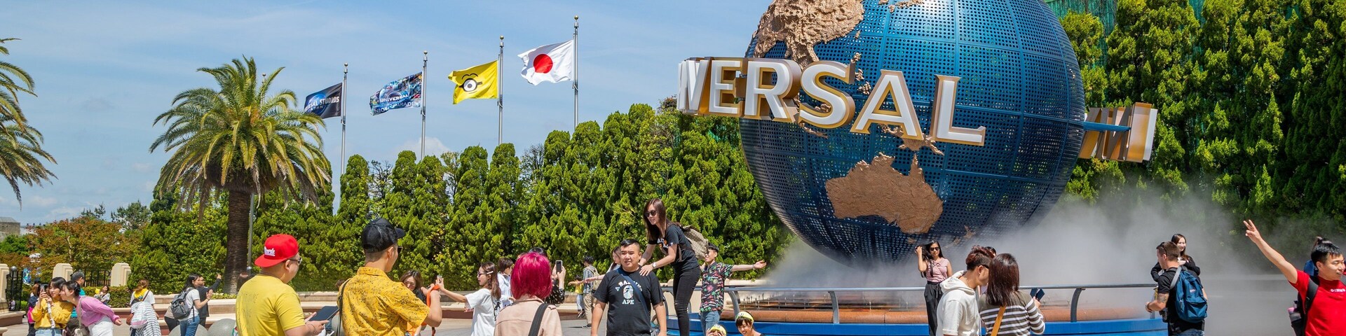 Un globo grande con 'VERSAL' y 'UNIVERSAL' escrito, rodeado de palmeras y gente.