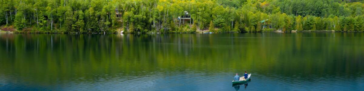 Father and daughter fishing in a canoe on a calm tranquil lake with a forest in the distance. Lac Lambert, Saint-Alexis-des-Monts, Quebec, Canada.