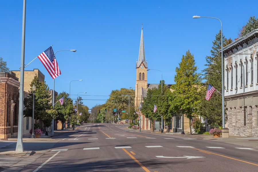 A street lined with American flags, a church with a steeple, and historic buildings.