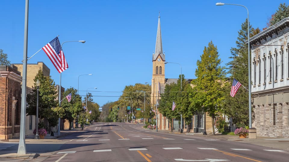 A street lined with American flags, a church with a steeple, and historic buildings.