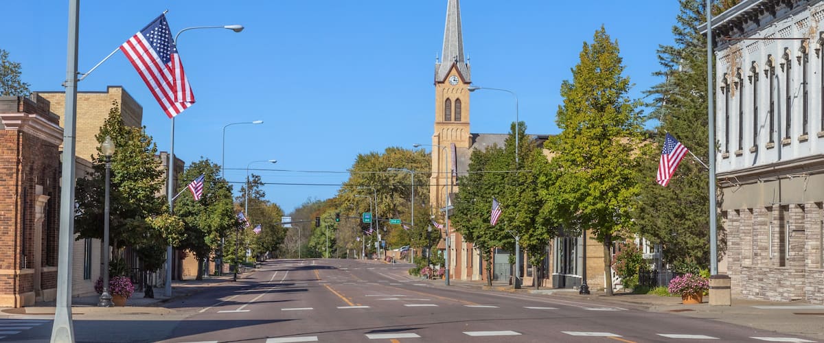 A street lined with American flags, a church with a steeple, and historic buildings.