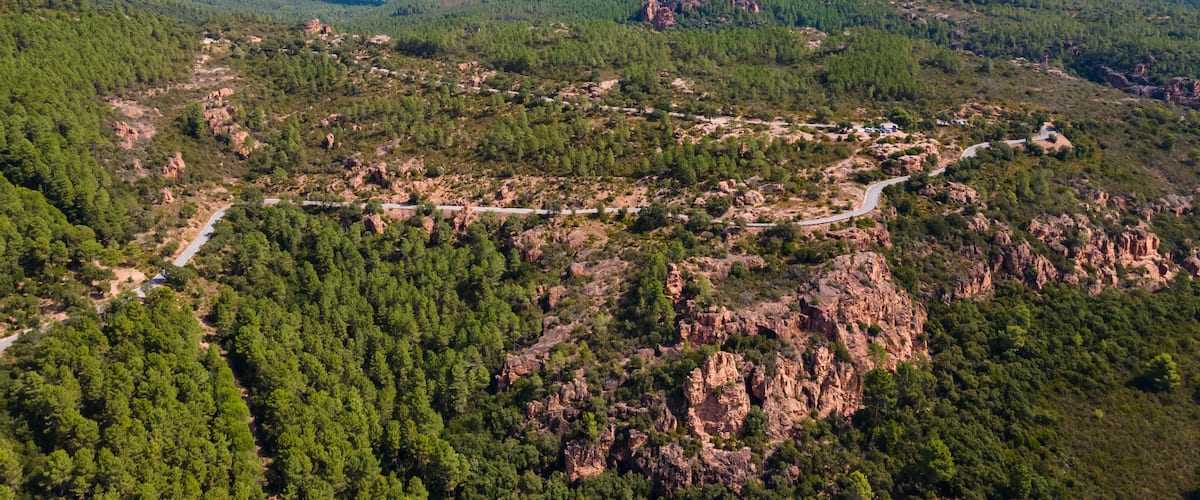 A mountainous landscape with a winding road, dense forests, and a prominent rocky peak.