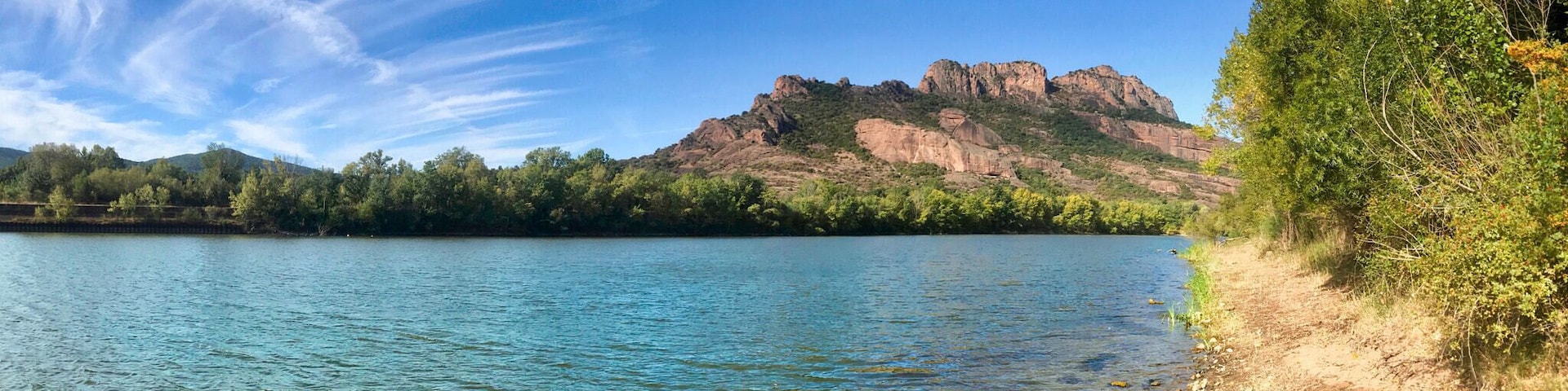 Un lago tranquilo con aguas cristalinas, rodeado de árboles y una montaña rocosa al fondo.