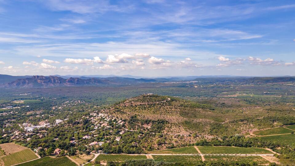 A mountainous landscape with a town nestled in the valley, vineyards, and distant mountains.
