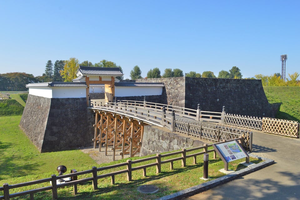 Une porte coréenne traditionnelle, avec un pont en bois, des murs de pierre et un ciel d’un bleu limpide.