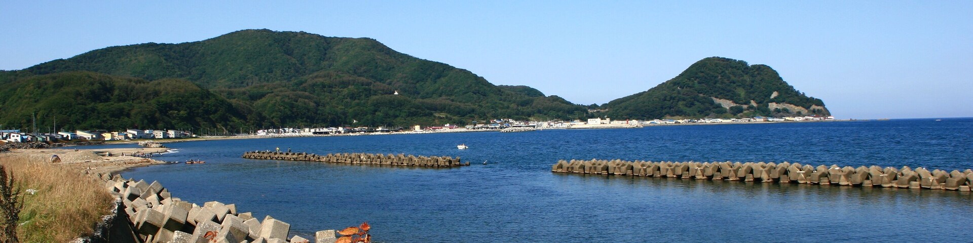 Eine Küstenlandschaft mit Strand, Felsen und grünen Hügeln im Hintergrund.