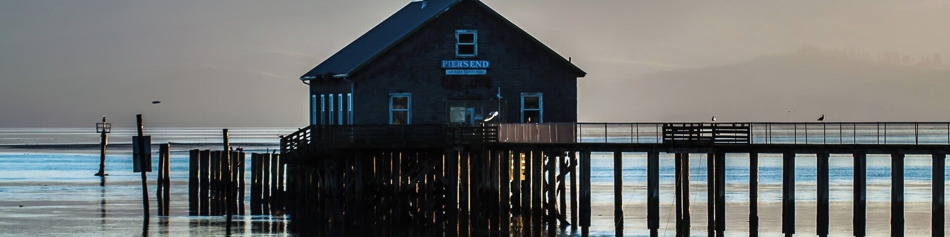 Un muelle de madera que se adentra en aguas tranquilas, con un edificio identificado como "Pier's End" al final.