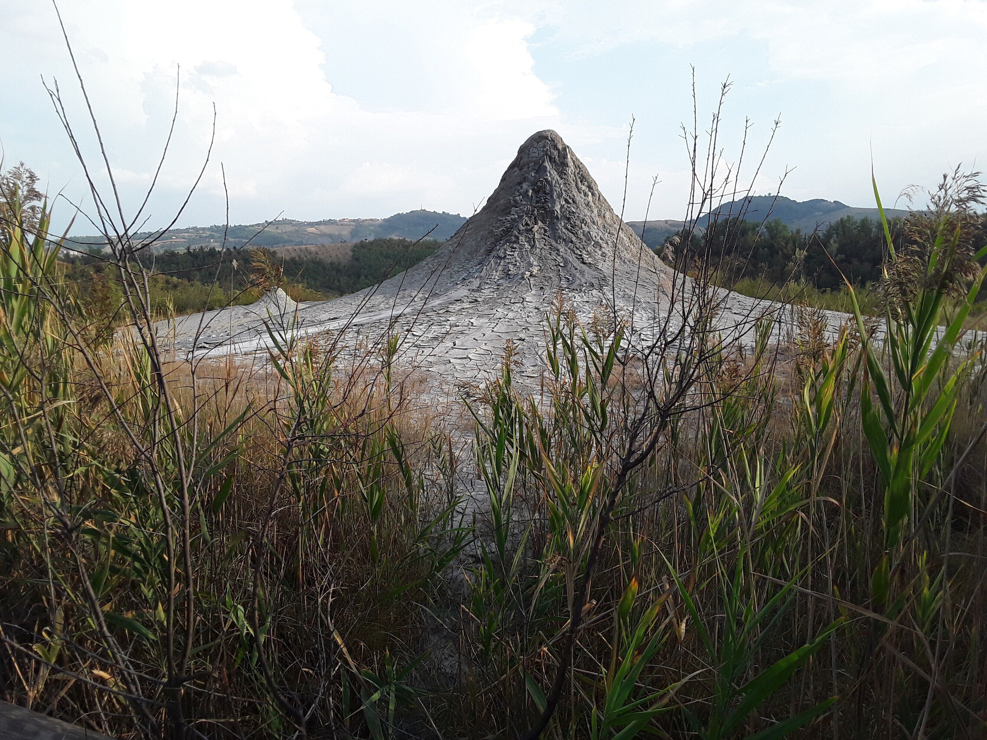 A large rock formation surrounded by tall grasses and hills in the background.