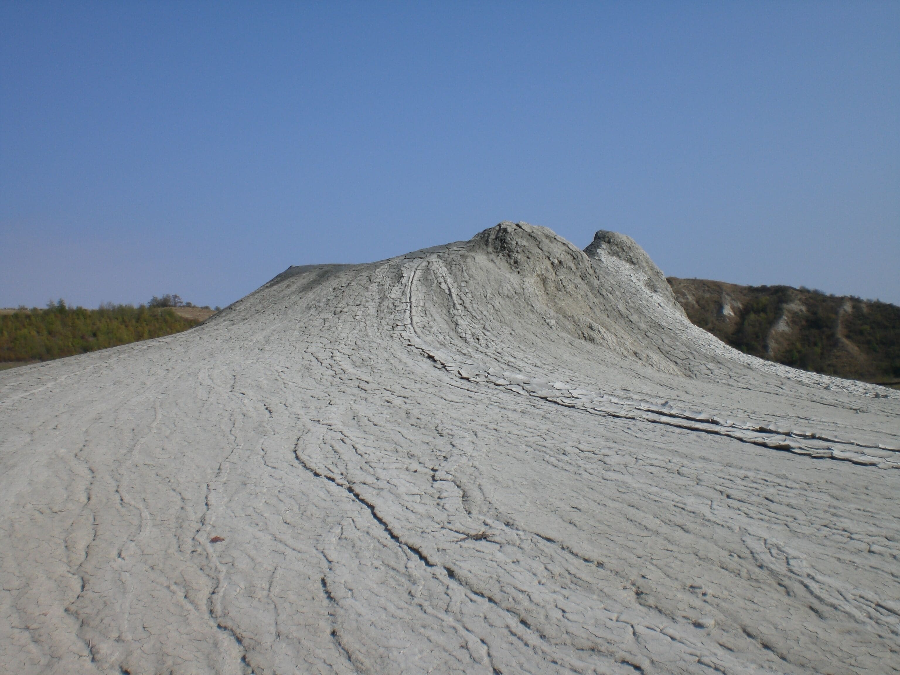 A dry, cracked landscape with a large mound of earth and a clear blue sky.