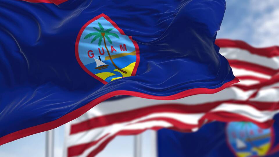 Flags of Guam waving in the wind with the US flag on a clear day