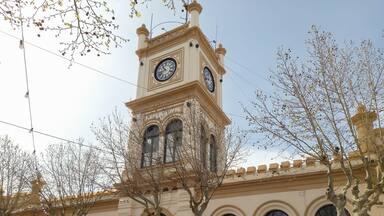 Um edifício histórico com uma torre do relógio, janelas em arco e uma porta central.