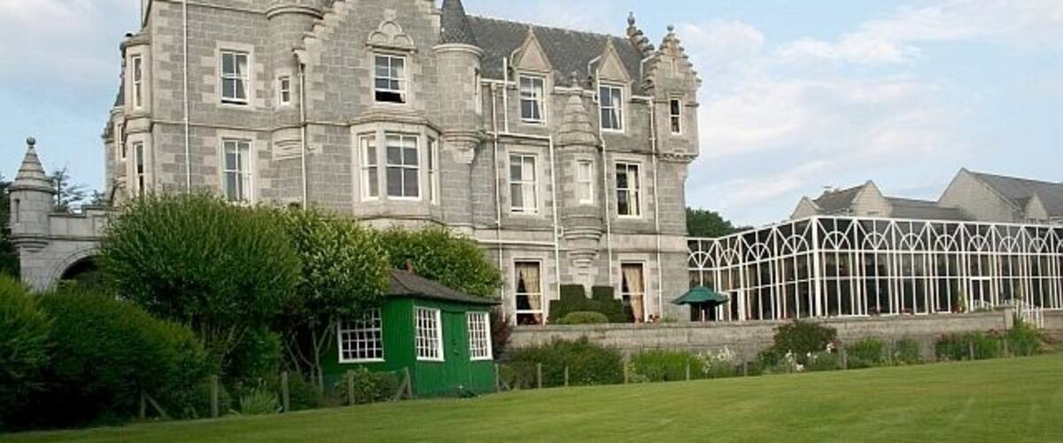 A large, historic stone building with multiple towers and a green outbuilding.
