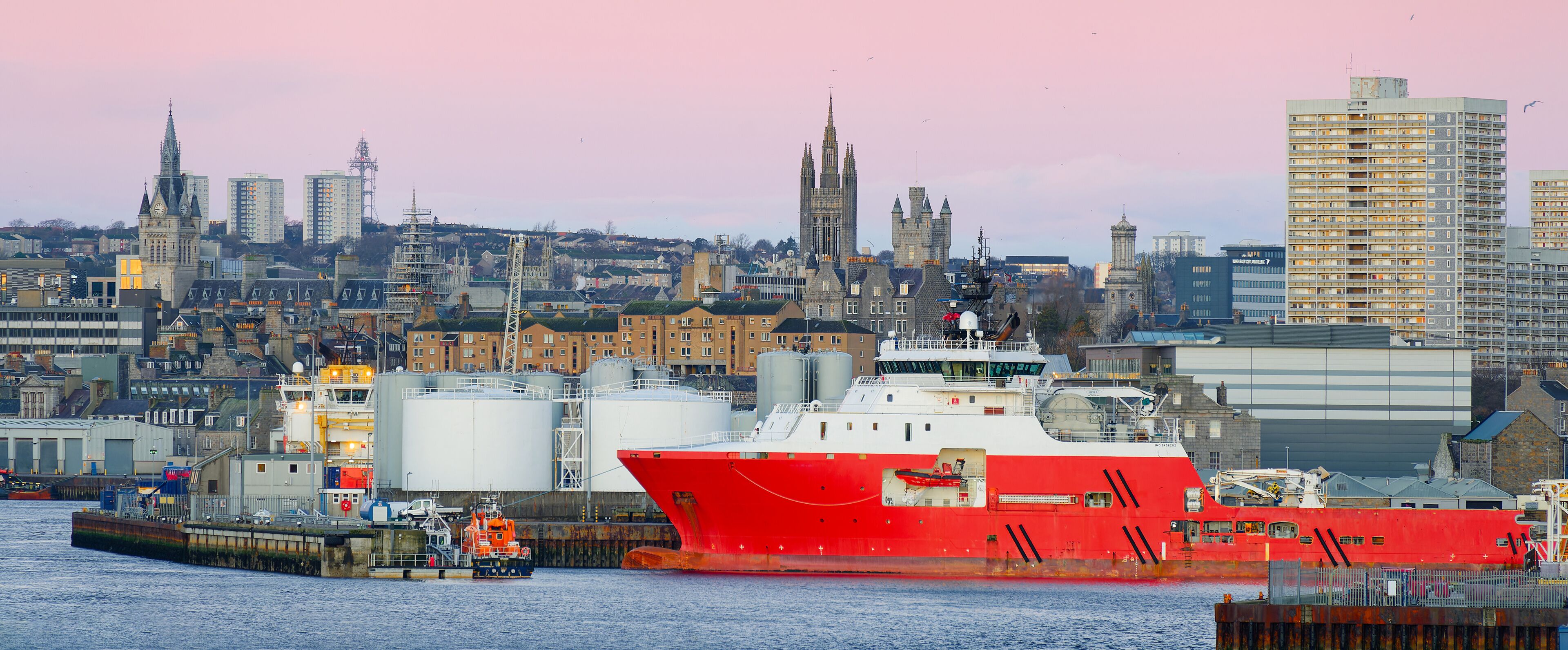 Un gran barco rojo amarrado en un puerto, con un horizonte urbano de fondo.