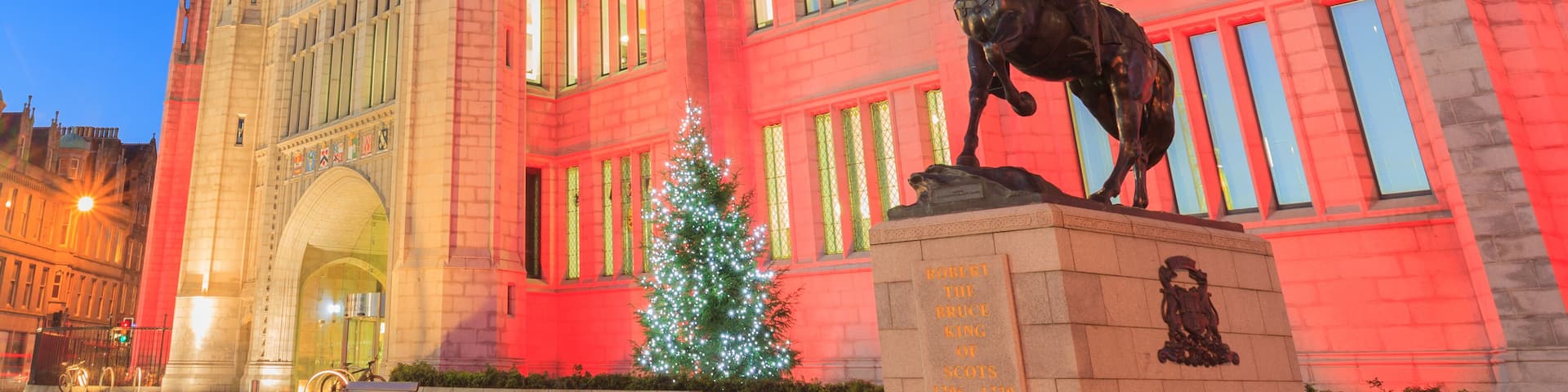 A historic building with Gothic architecture, a statue of a mounted figure, and a Christmas tree.