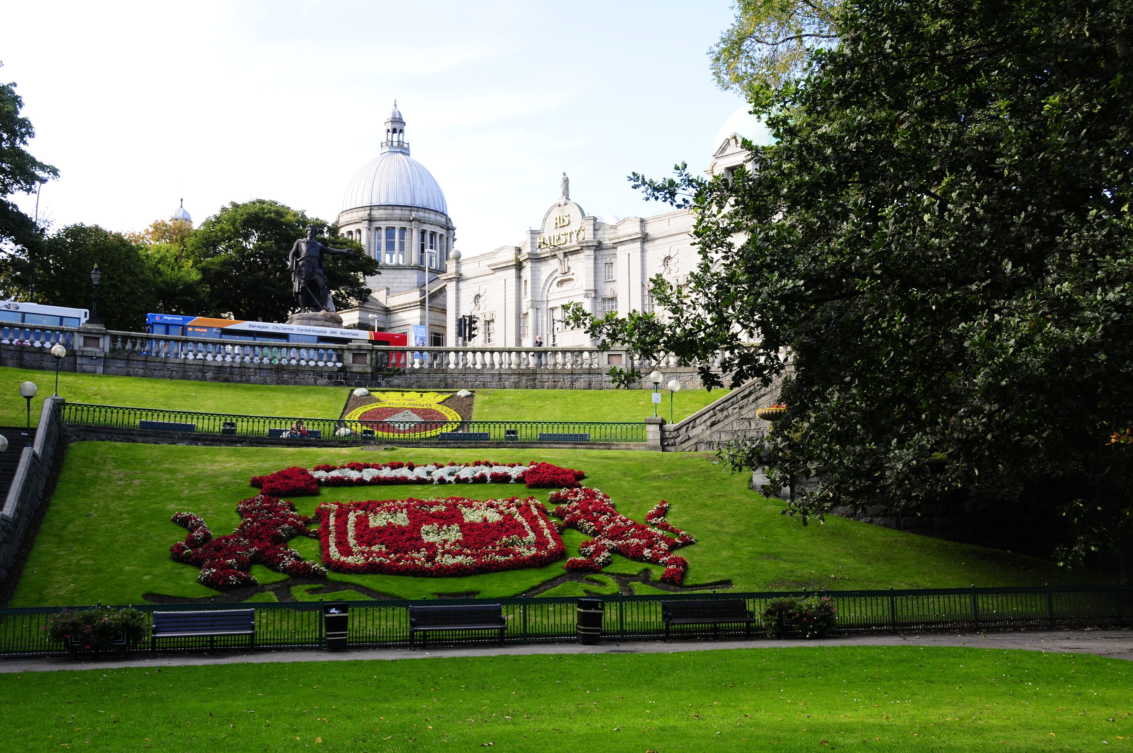 A landscaped garden with a statue, a large building with a dome, and a tree.