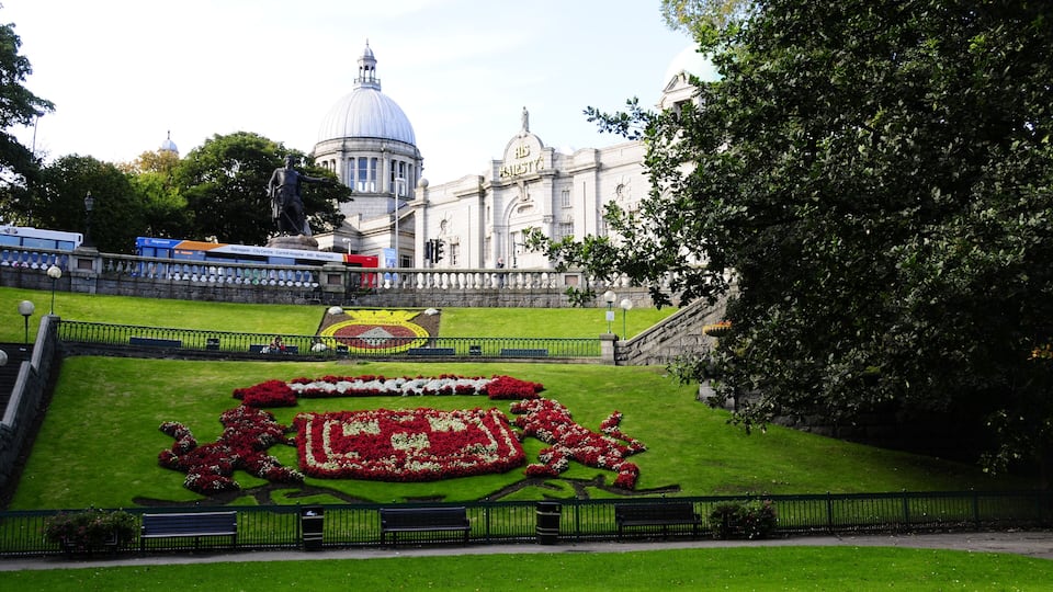 A landscaped garden with a statue, a large building with a dome, and a tree.