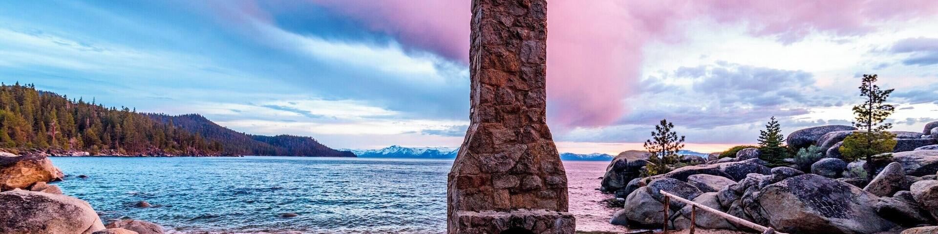 A stone structure on a beach with a lake and mountains in the background.