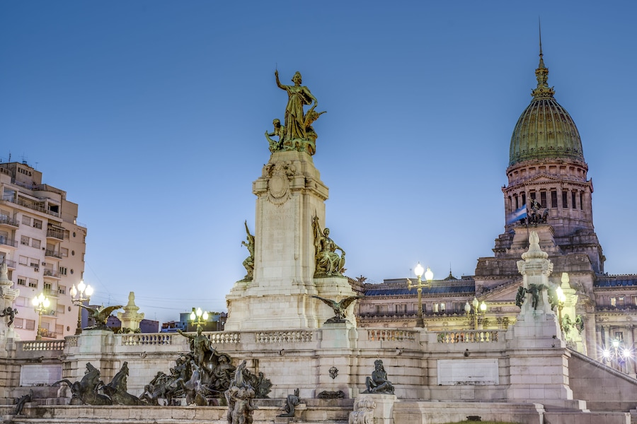 A large equestrian statue, a domed building, and a cityscape at dusk.