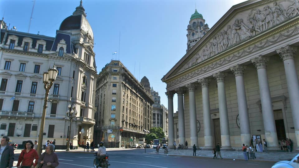 A city street with classical architecture, including a building with columns and a dome.
