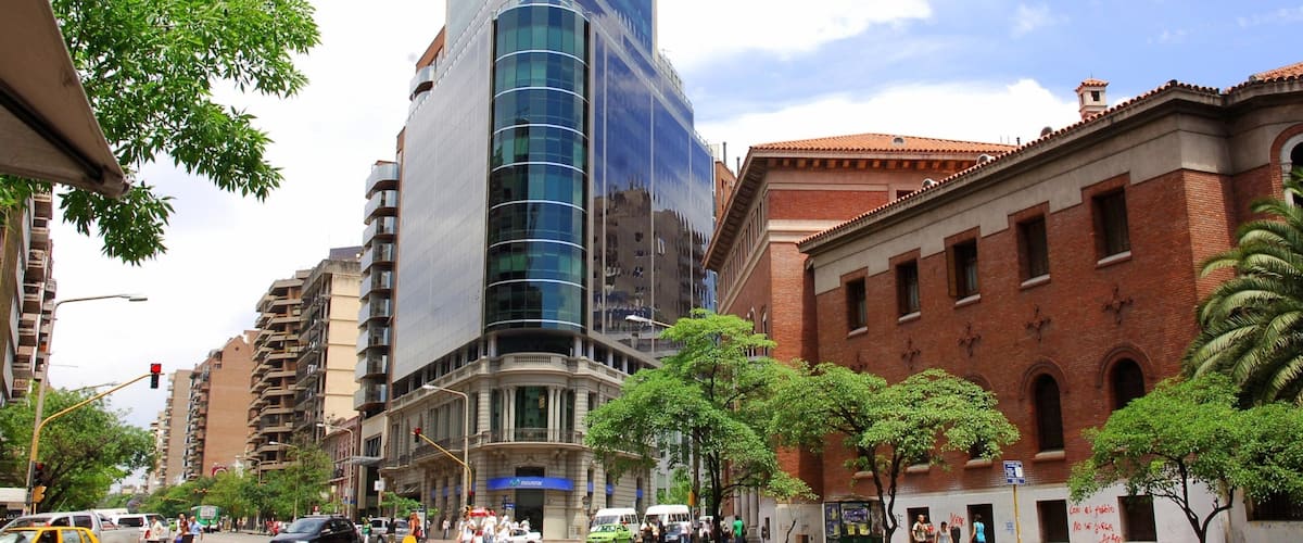 A modern building with a glass facade, a traditional brick building, and a busy street with pedestrians and vehicles.
