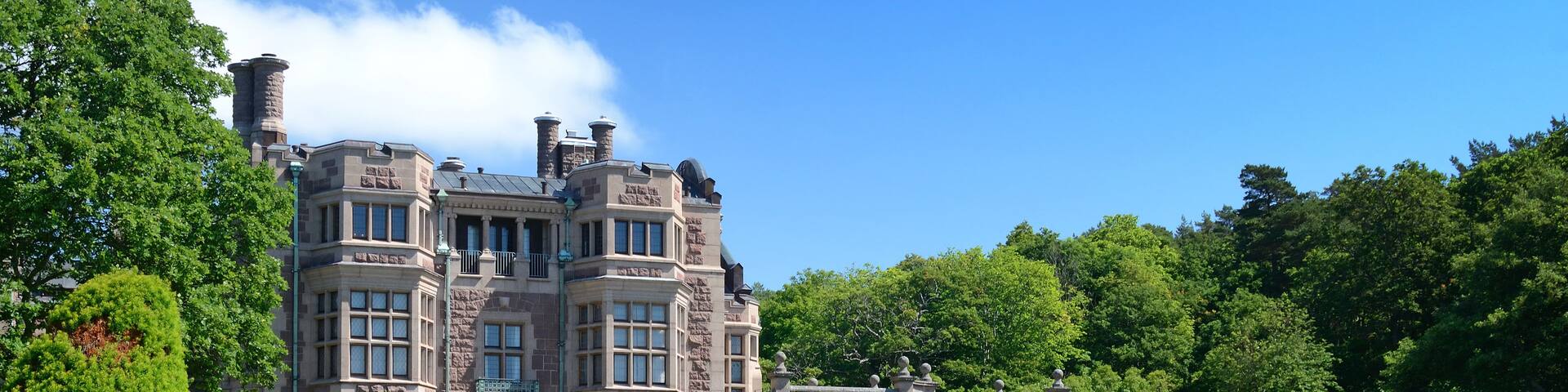A large, historic stone building with a formal garden and trimmed hedges.