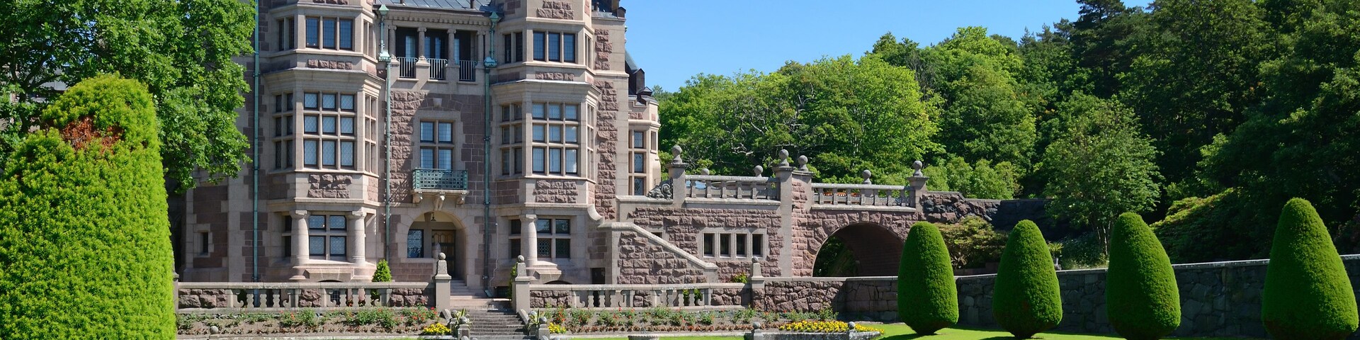 Un edificio grande y antiguo de piedra con un jardín formal y setos podados.