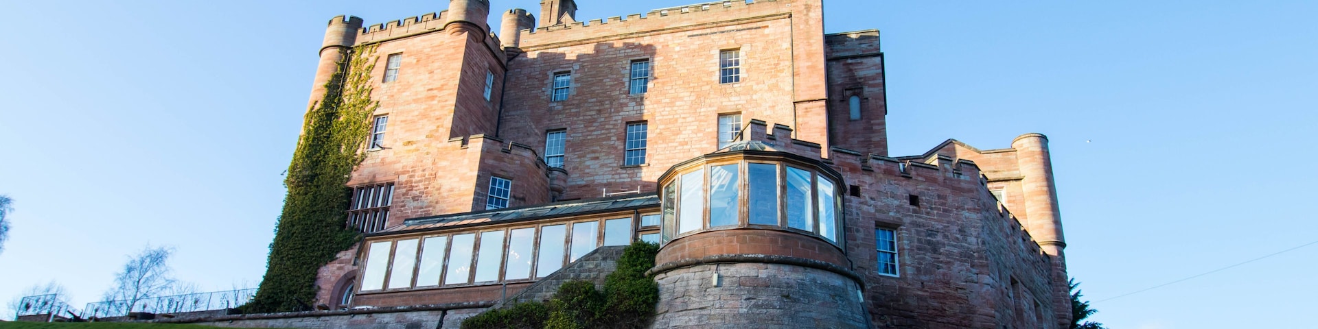 A large, historic castle with multiple towers and a prominent turret, situated on a grassy hill.