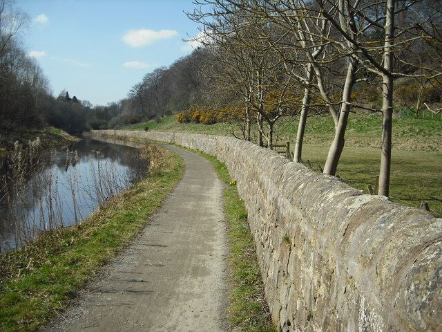 A narrow path beside a river, flanked by stone walls and leafless trees.