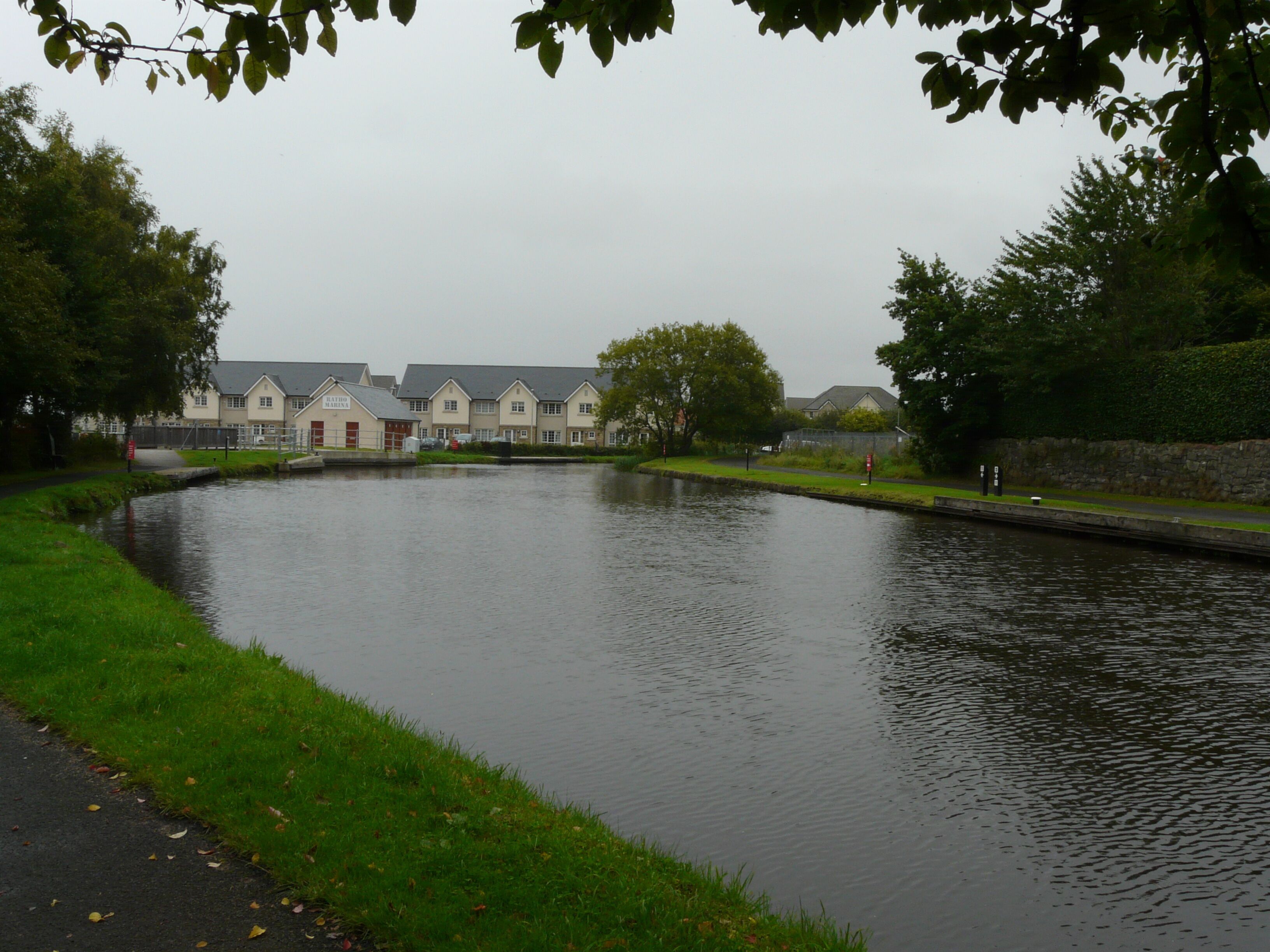 A calm river with a bridge, surrounded by greenery and a row of houses.