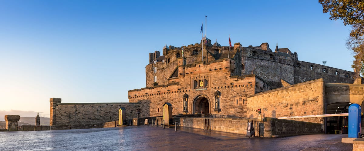 A historic stone castle with battlements, a flagpole, and a clear sky.